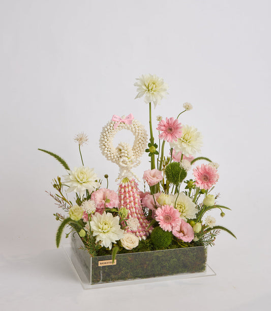Elegant floral arrangement featuring cream and pink gerberas, dahlias, and carnations in a gray rectangular planter with moss base and clear acrylic stand.