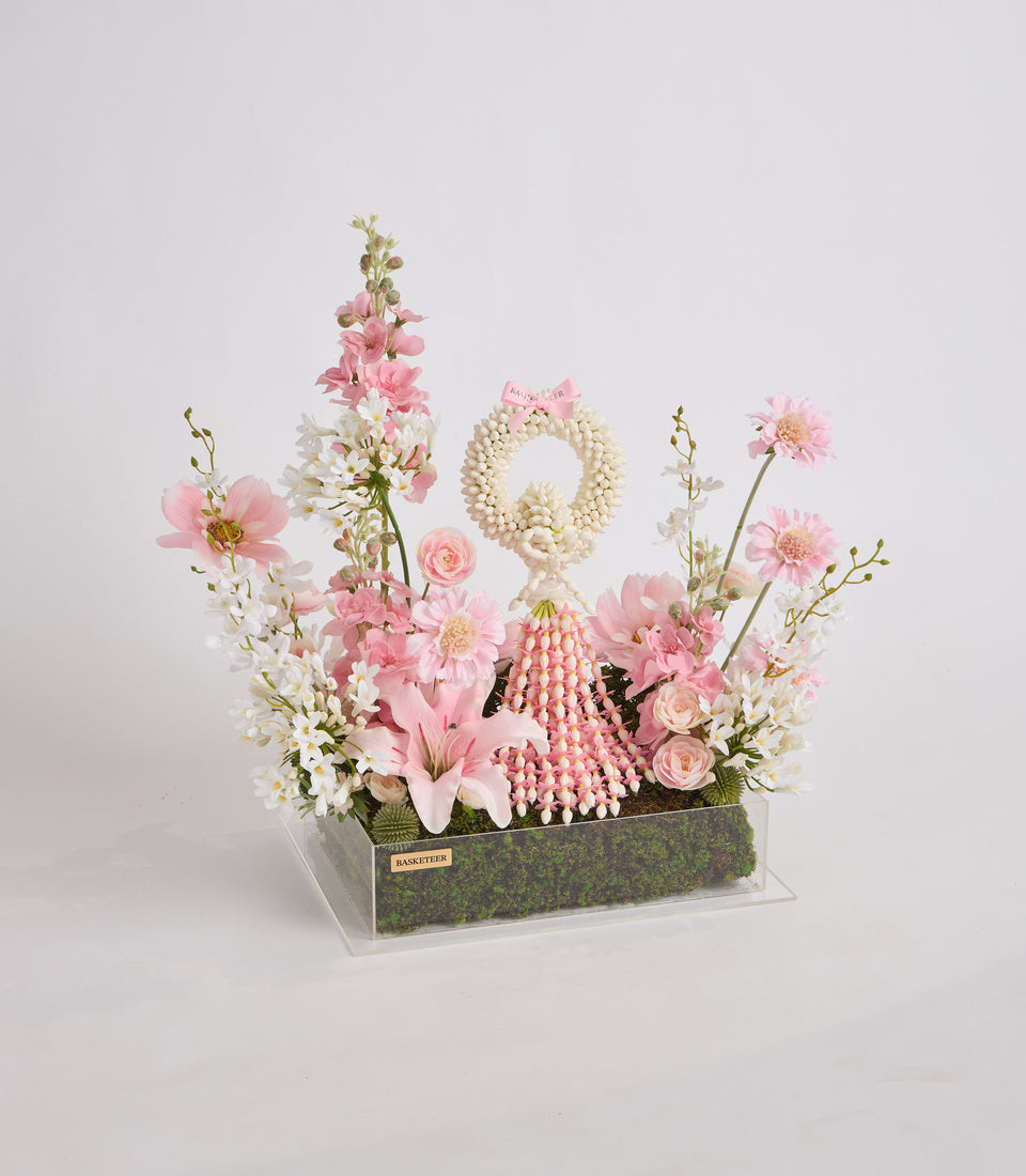 Elegant floral arrangement in clear acrylic box with pink and white flowers, pearl wreath, beaded details, and moss base. Luxury gift presentation.