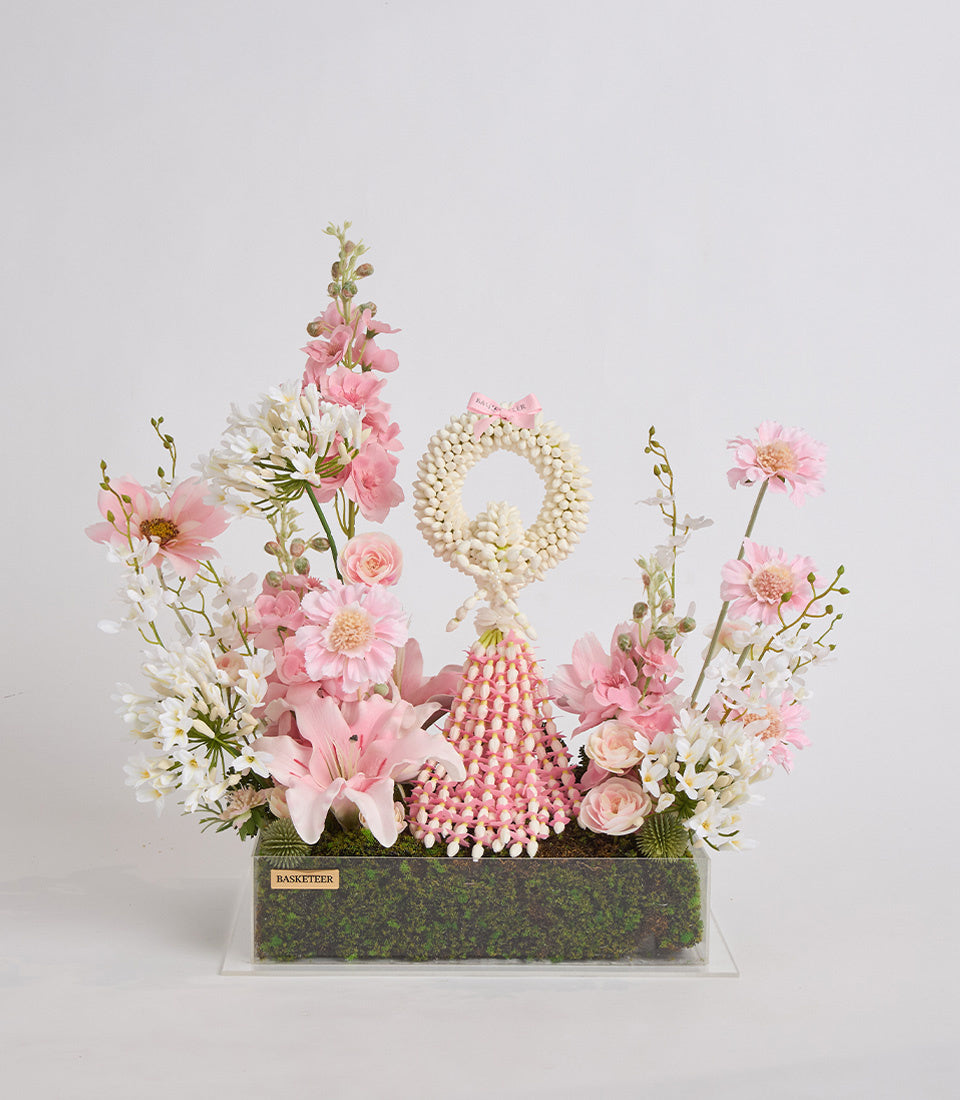 Luxurious floral arrangement with pink gerberas, roses, white daisies, pearl beaded number 9, and coral spike flower in moss-lined acrylic box.