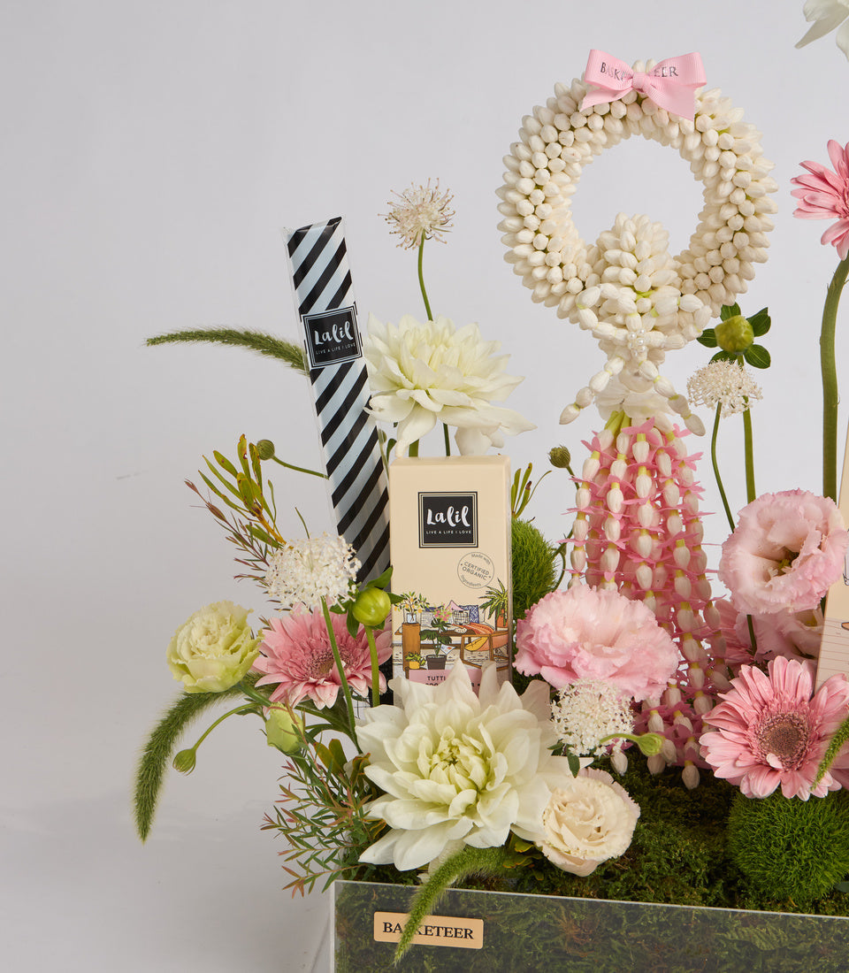 Luxe floral arrangement with pink and white flowers, cream pearl wreath, striped gift box, and candle in dark container.