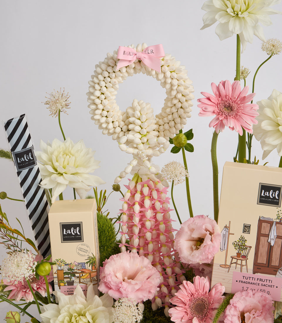 Lalif fragrance gift set with cream packaging surrounded by pink and white flowers, a cream pearl beaded wreath with pink bow, and striped tissue paper on white background.