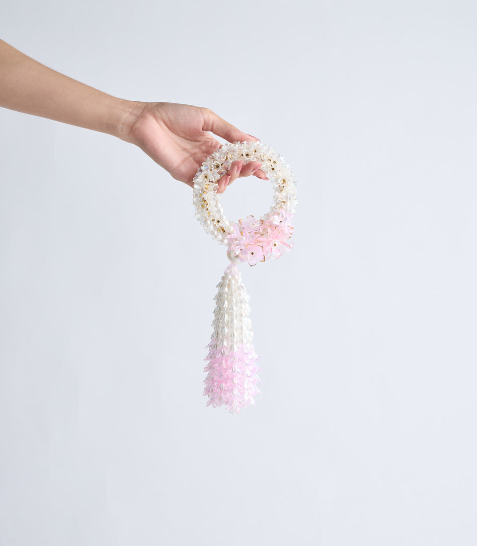 Hand holding a delicate beaded bracelet with cream and pink beads, featuring a pink flower charm and matching tassel detail.