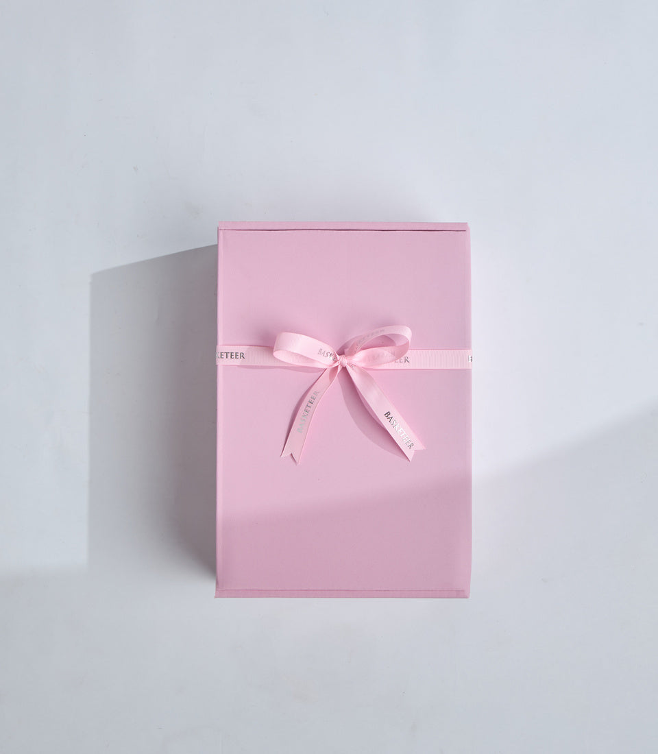 Pink gift box with satin ribbon bow and text detail on white background, minimal luxury packaging style.
