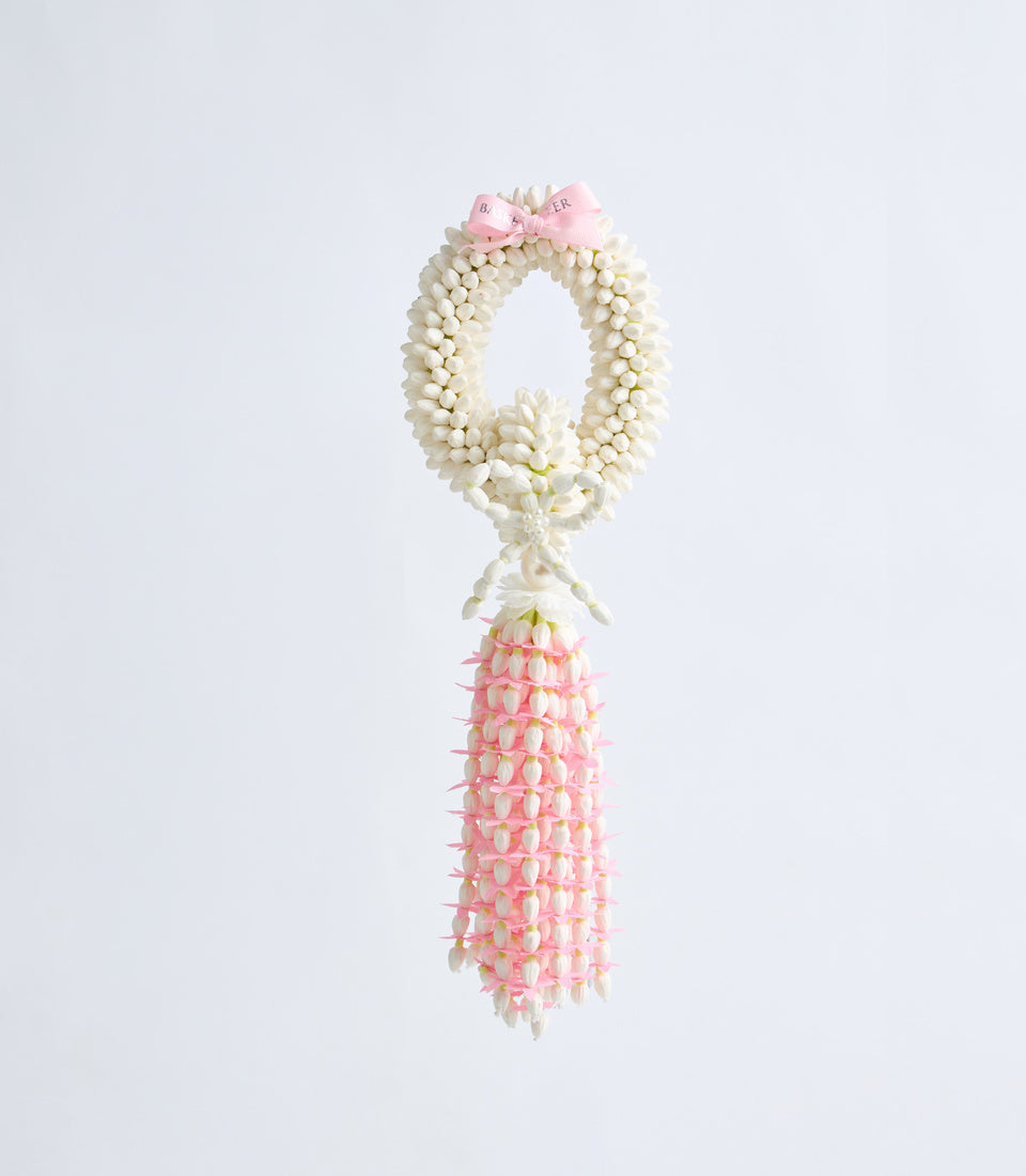 Garland lei necklace with cream jasmine buds forming oval loop and pink tuberose flowers cascading down, adorned with pink ribbon bow.