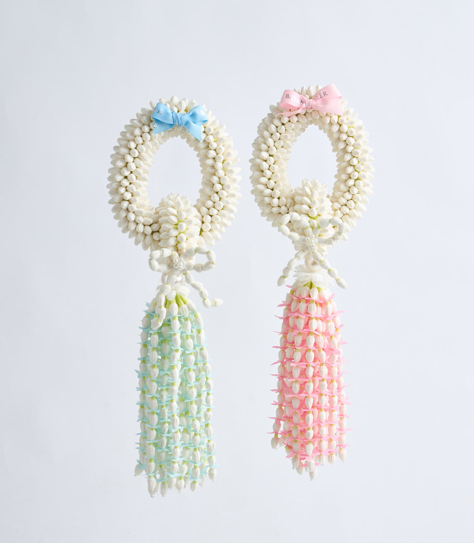 Two decorative flower garland leis with cream beaded loops, small ribbon bows, and cascading floral tassels in green and pink.
