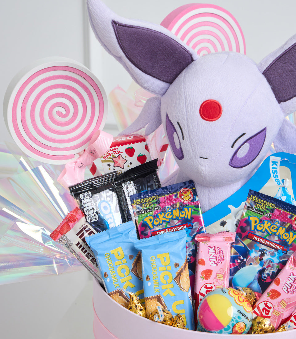 # Alt Text

Pokémon Espeon plush toy surrounded by pink and white spiral lollipops, Pokémon trading cards, cookies, and colorful candies in a pink gift basket.