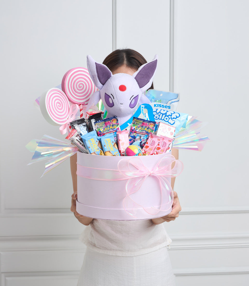 Pink cylindrical gift box with white plush cat character, purple spiral lollipops, colorful candies, and iridescent ribbons.