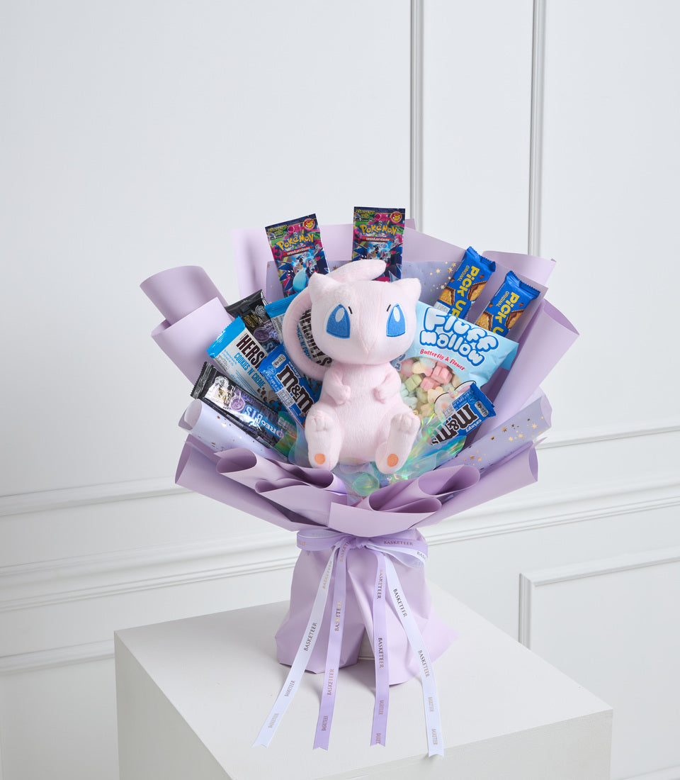 Pink plush Pokémon bouquet with candies, trading cards, and sweets arranged in lavender tissue paper with ribbon bow.