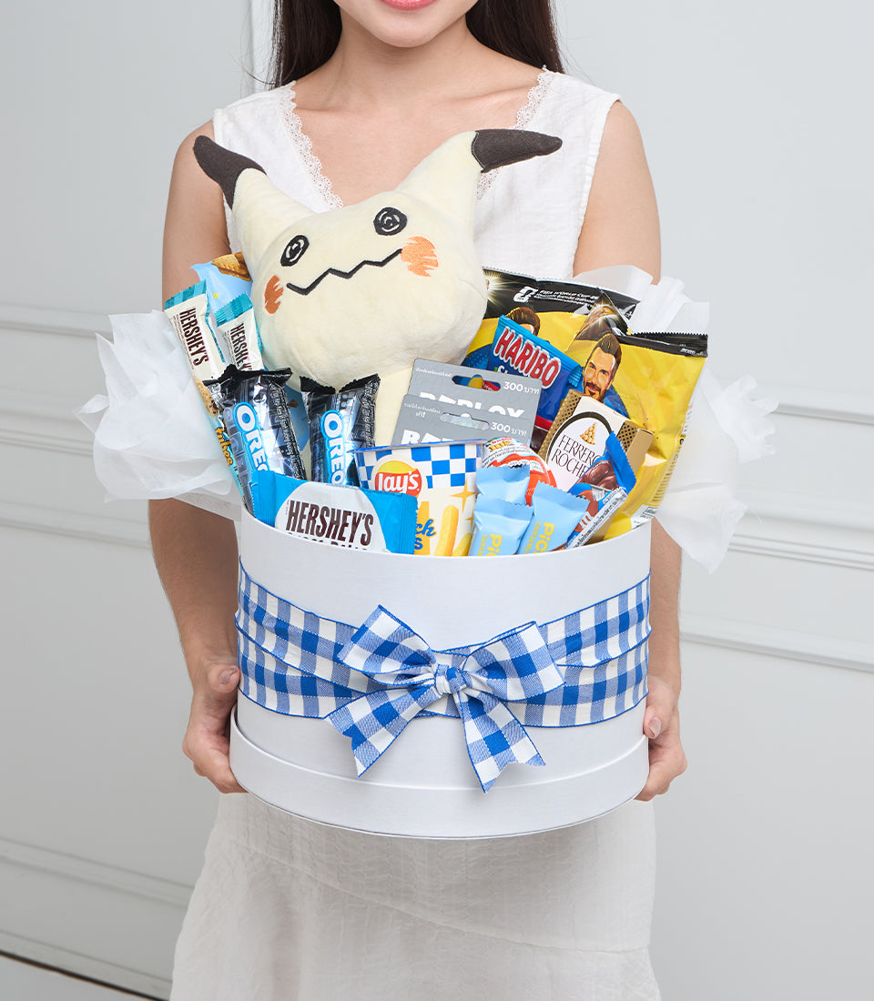 # Gift Basket with Pikachu Plush and Snacks

Woman holding white cylindrical gift basket with blue gingham bow, filled with Pikachu plush toy, candies, chips, and snacks.