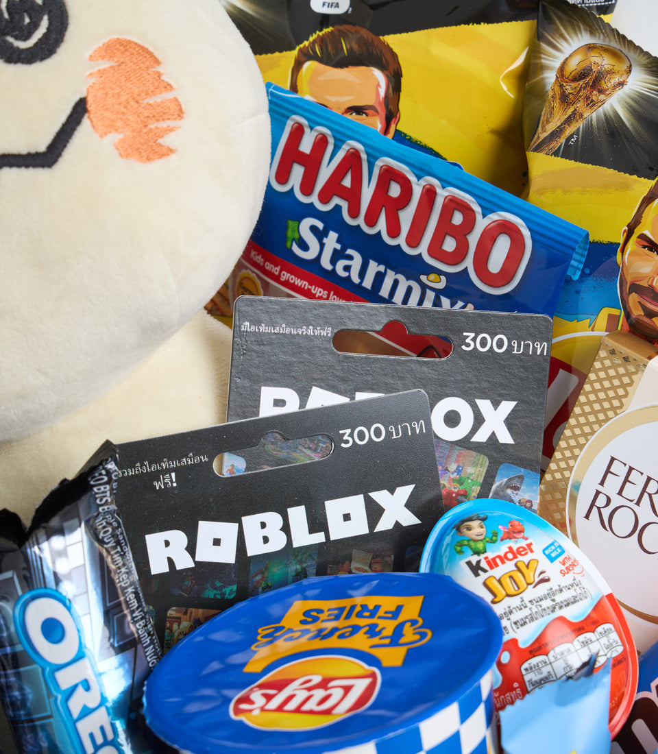 Roblox and FIFA-themed gift collection featuring game cards, Haribo candy, Kinder Joy, sports drinks, and merchandise on white textile background.