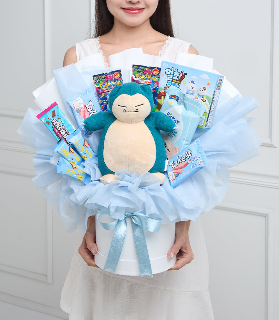 Woman holding blue Snorlax plush surrounded by Pokemon candy and toys in light blue tulle bouquet with ribbon bow.