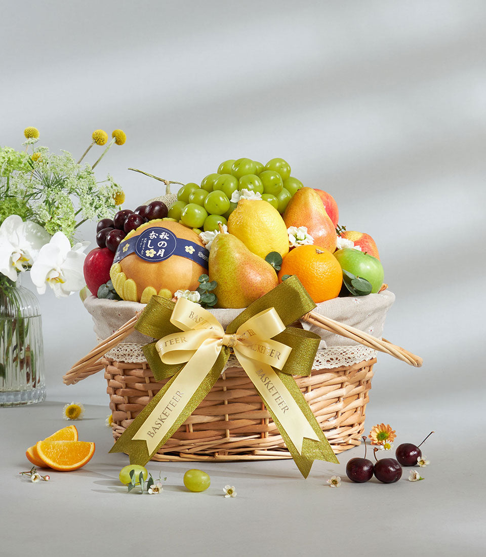 Premium wicker fruit basket with fresh grapes, pears, apples, and oranges, tied with cream ribbon