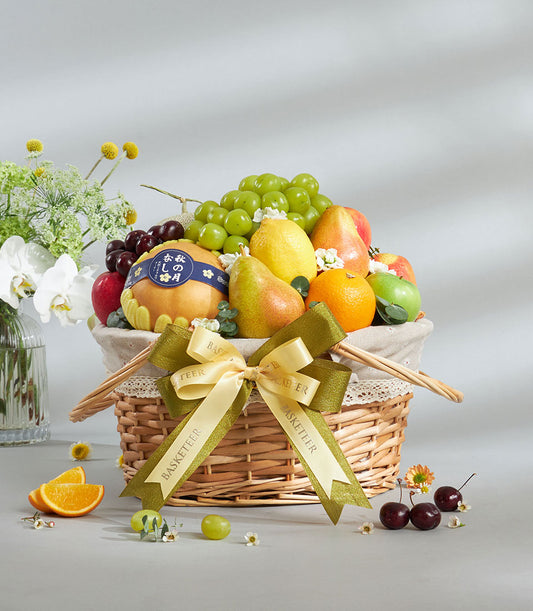 Premium wicker fruit basket with fresh grapes, pears, apples, and oranges, tied with cream ribbon