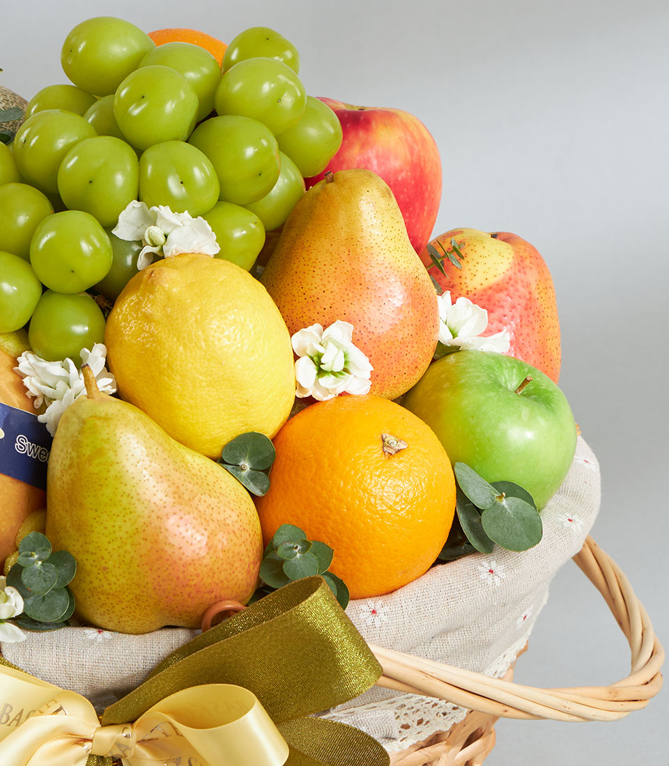 Premium imported fruit basket with grapes, pears, apples, oranges, and lemons, finished with eucalyptus and white flowers