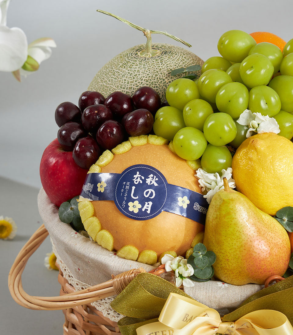 Woven wicker fruit basket with fresh cantaloupe, grapes, cherries, pears, and imported nashi pear, tied with gold ribbon