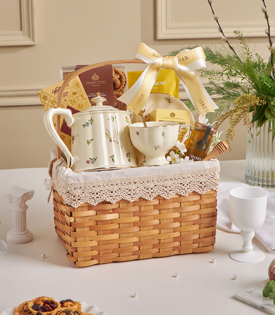 Cream ceramic teapot and teacup gift basket with British bakery treats, honey, and lace-trimmed woven wood for New Year