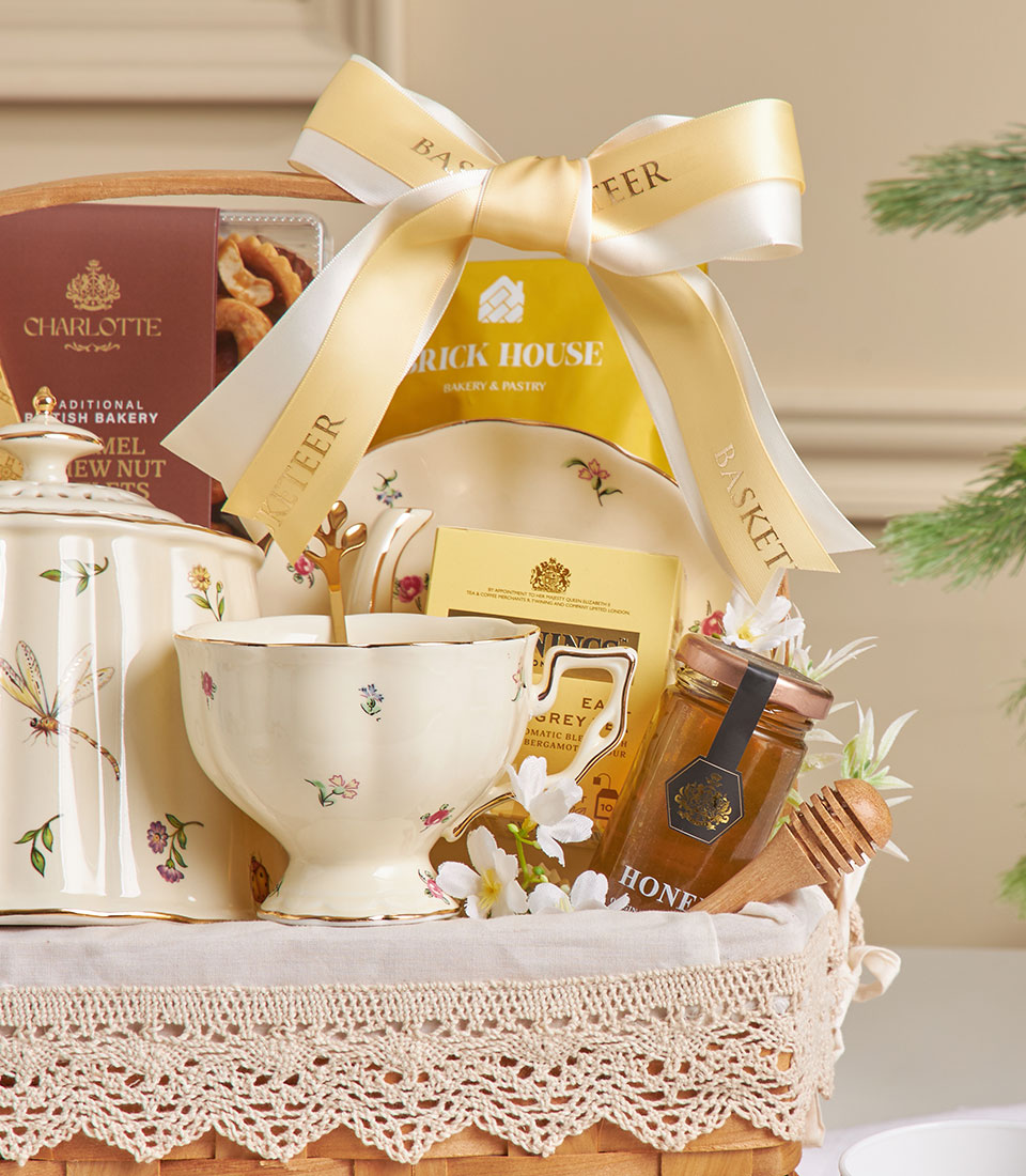 English tea time ceramic hamper with teapot, Earl Grey tea, honey, and pastries in woven basket with gold ribbon