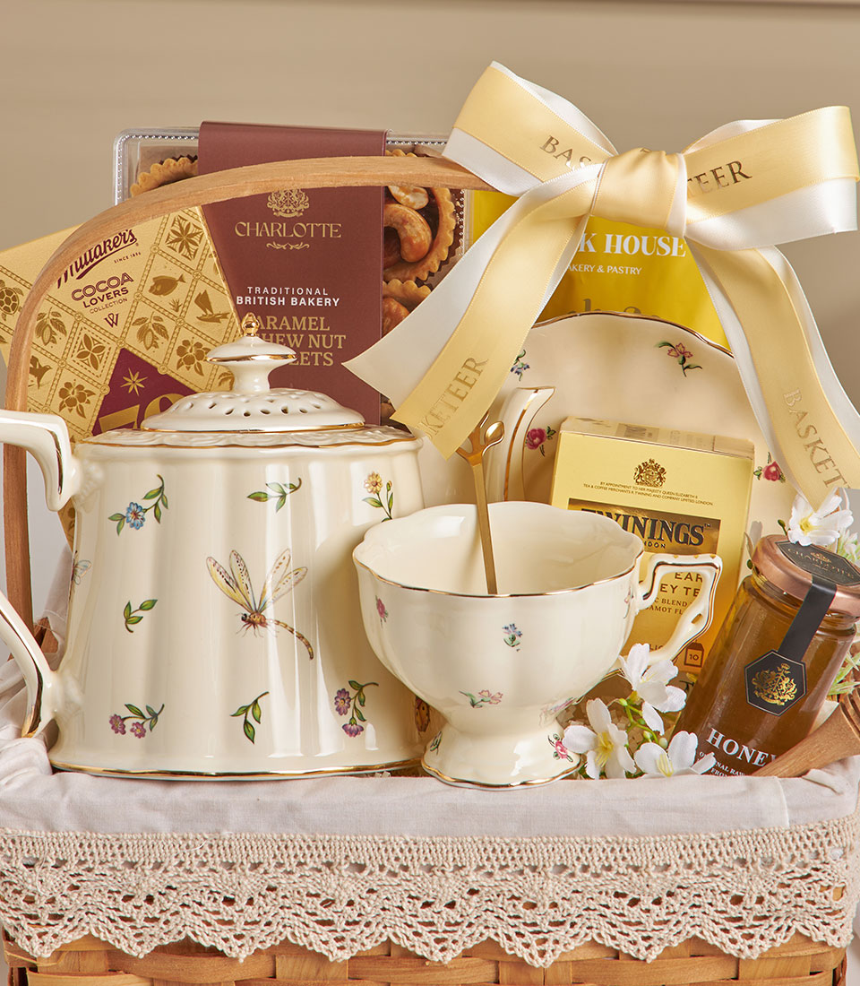 English tea time ceramic hamper with teapot, teacup, cookies, cashews, honey, and gold-trimmed florals in woven basket