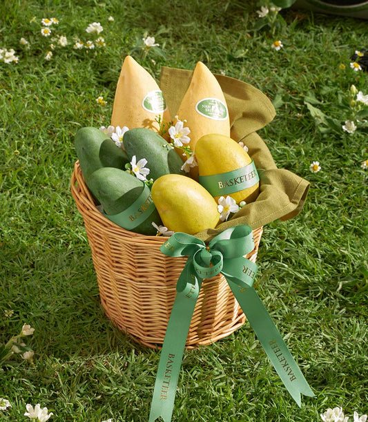 Woven wicker basket filled with premium Thai yellow and green mangoes, wrapped with green ribbons and white flowers