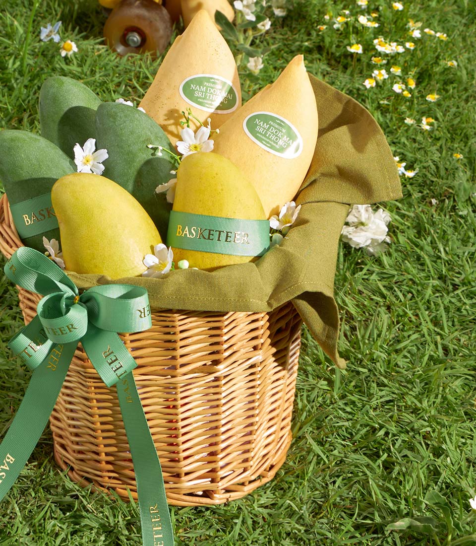 Premium Thai Nam Dok Mai mangoes in woven wicker basket with green ribbon and white florals