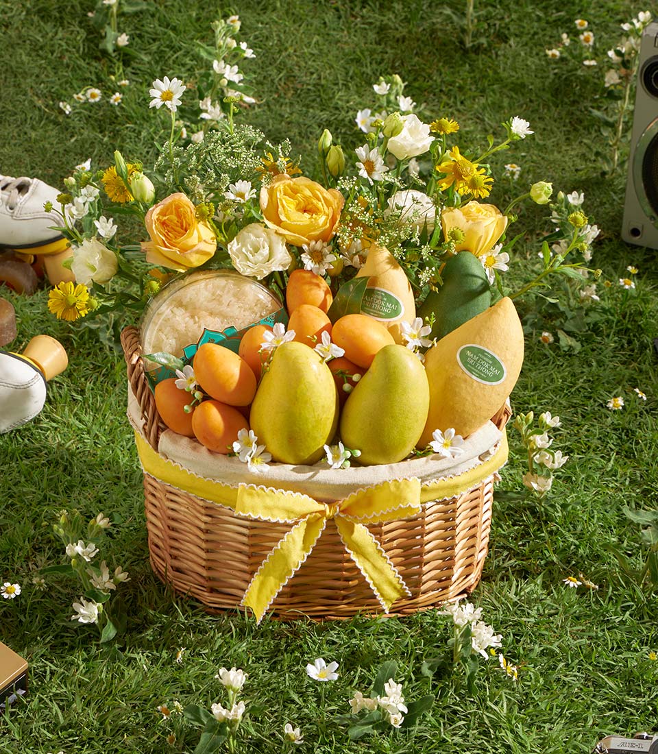Luxury tropical fruit and flower gift basket with yellow roses, mangoes, pears, and sticky rice on wicker with yellow ribbon