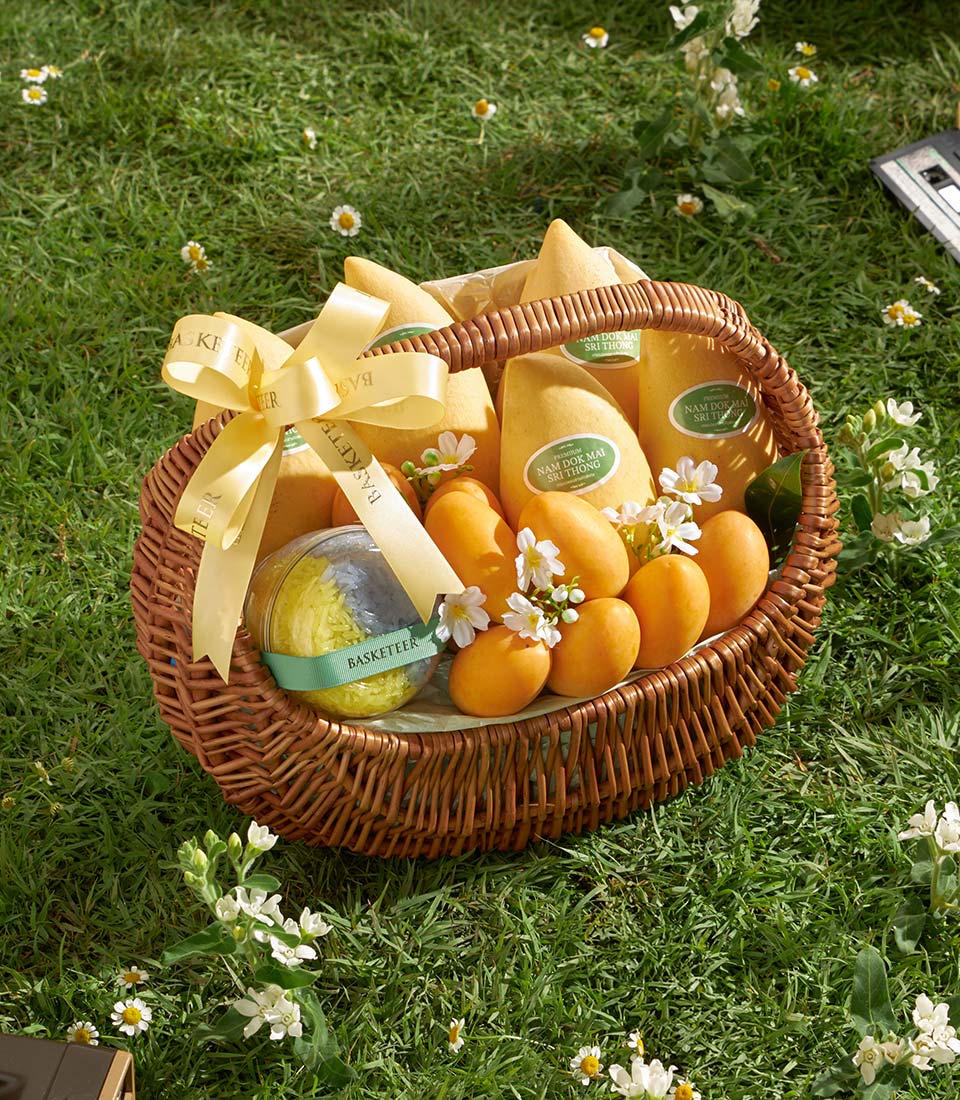 Woven wicker basket filled with ripe Nam Doc Mai mangoes and mayongchid oranges with sticky rice in spherical container