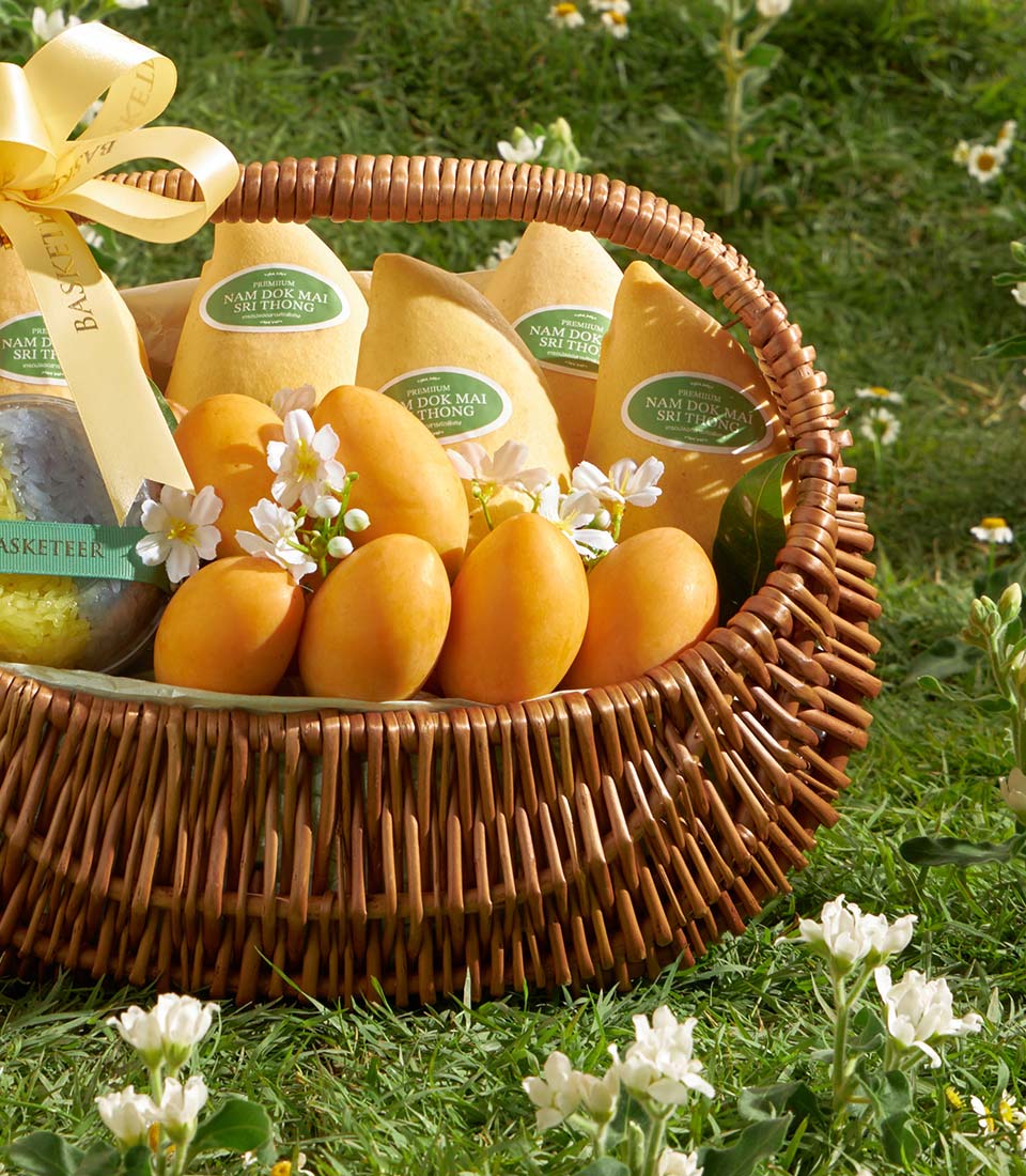 Woven basket filled with premium Nam Dok Mai mangoes, mango treats, and white flowers with golden Basketeer ribbon