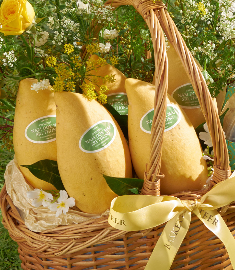 Premium Nam Dok Mai mango gift basket with fresh white flowers and green foliage in woven wicker