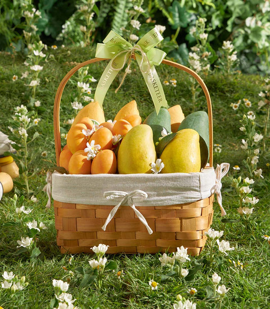 Woven wooden basket filled with fresh Thai mangoes, pears, and apricots with green ribbon bow