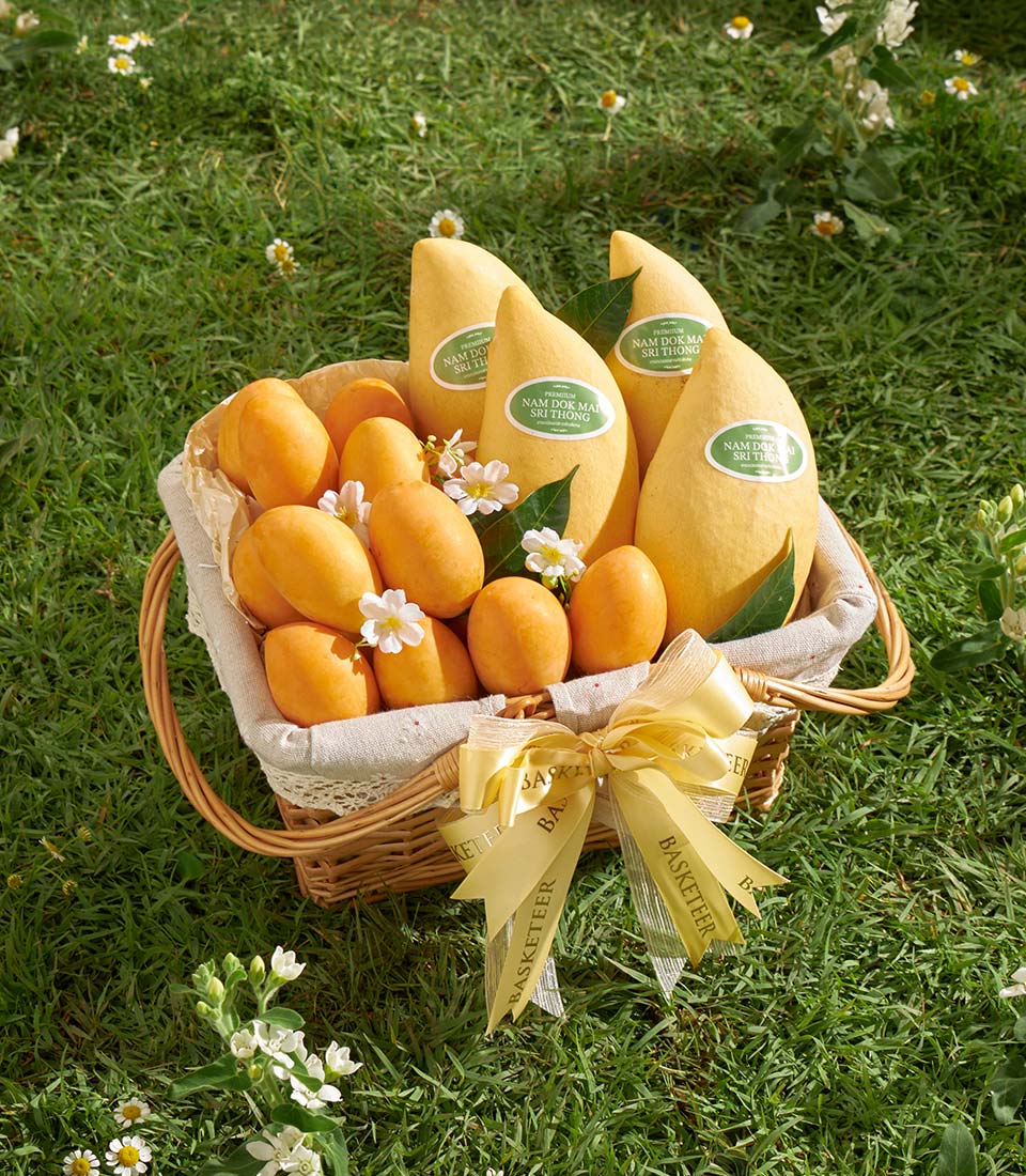 Luxury wicker fruit basket with golden ribbon, ripe Nam Dok Mai mangoes and Mayongchid fruits, fresh florals