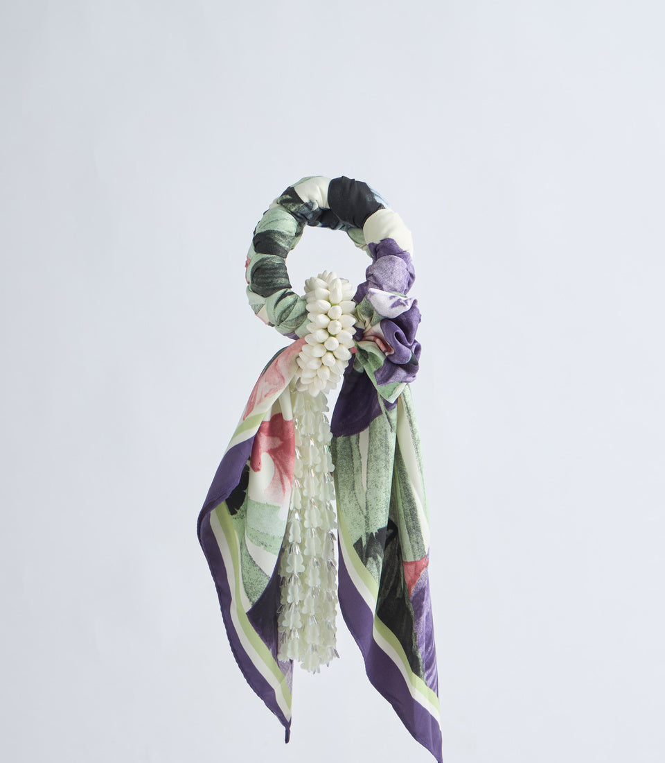 Decorative fabric scrunchie with floral design featuring white flowers, purple, green, and pink hues with hanging tail ribbons.