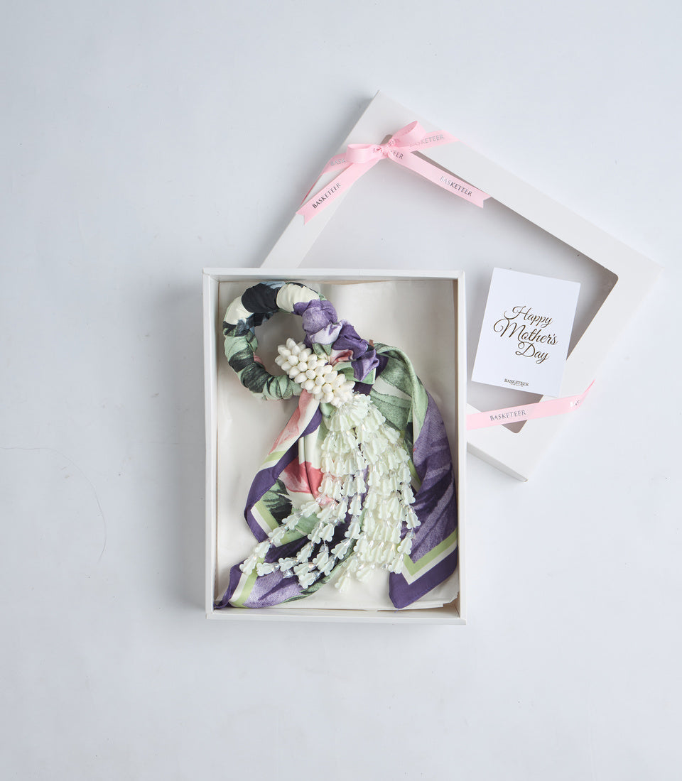 Luxury Mother's Day gift set featuring a decorative silk scarf with purple, green and pink florals, white flowers, paired with greeting card and pink ribbon bow.