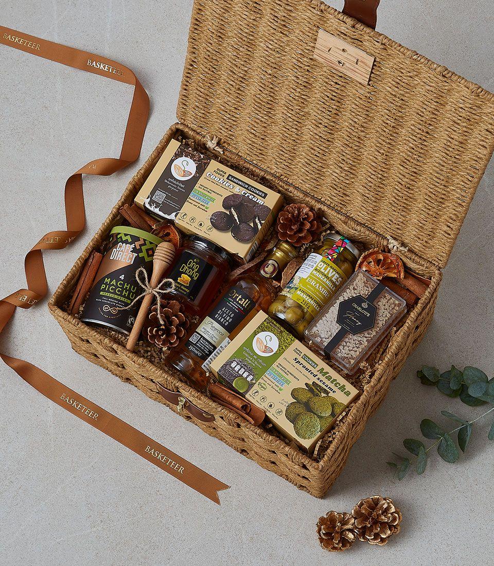 Premium wicker hamper filled with gourmet cookies, honey, coffee, olives, and artisan treats with gold pinecones and cinnamon