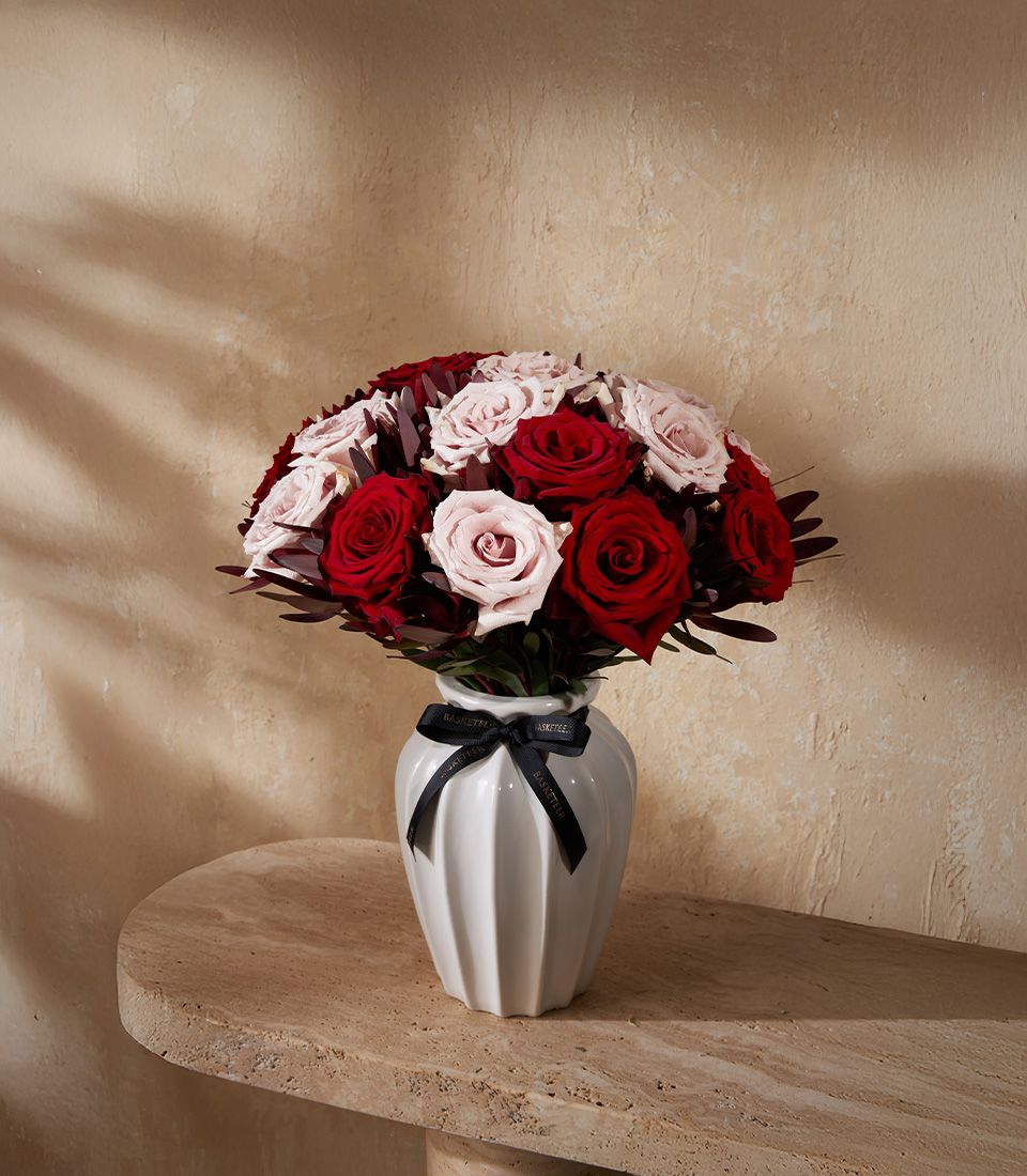 Red and light pink rose bouquet in white ceramic fluted vase with black ribbon