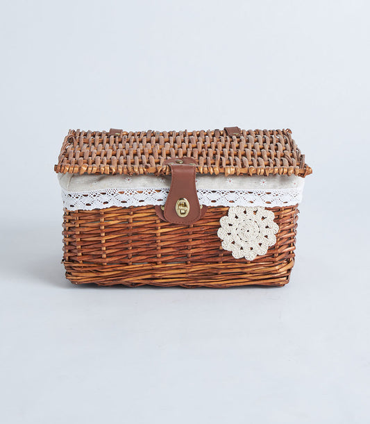 Handwoven rectangular wicker storage basket with beige fabric trim, leather strap, and crocheted flower accent