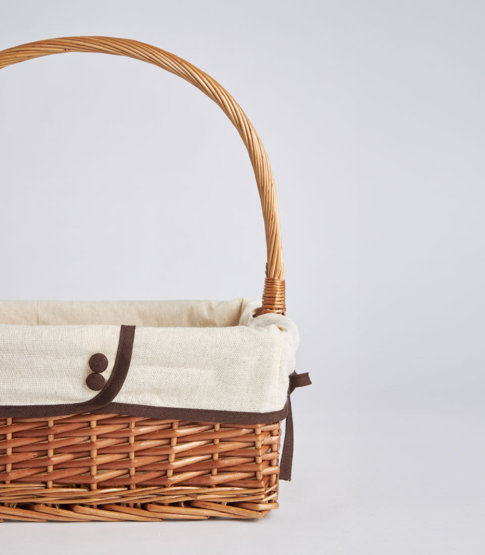 Light brown woven wicker basket with cream fabric liner and arched handle for premium gift hampers