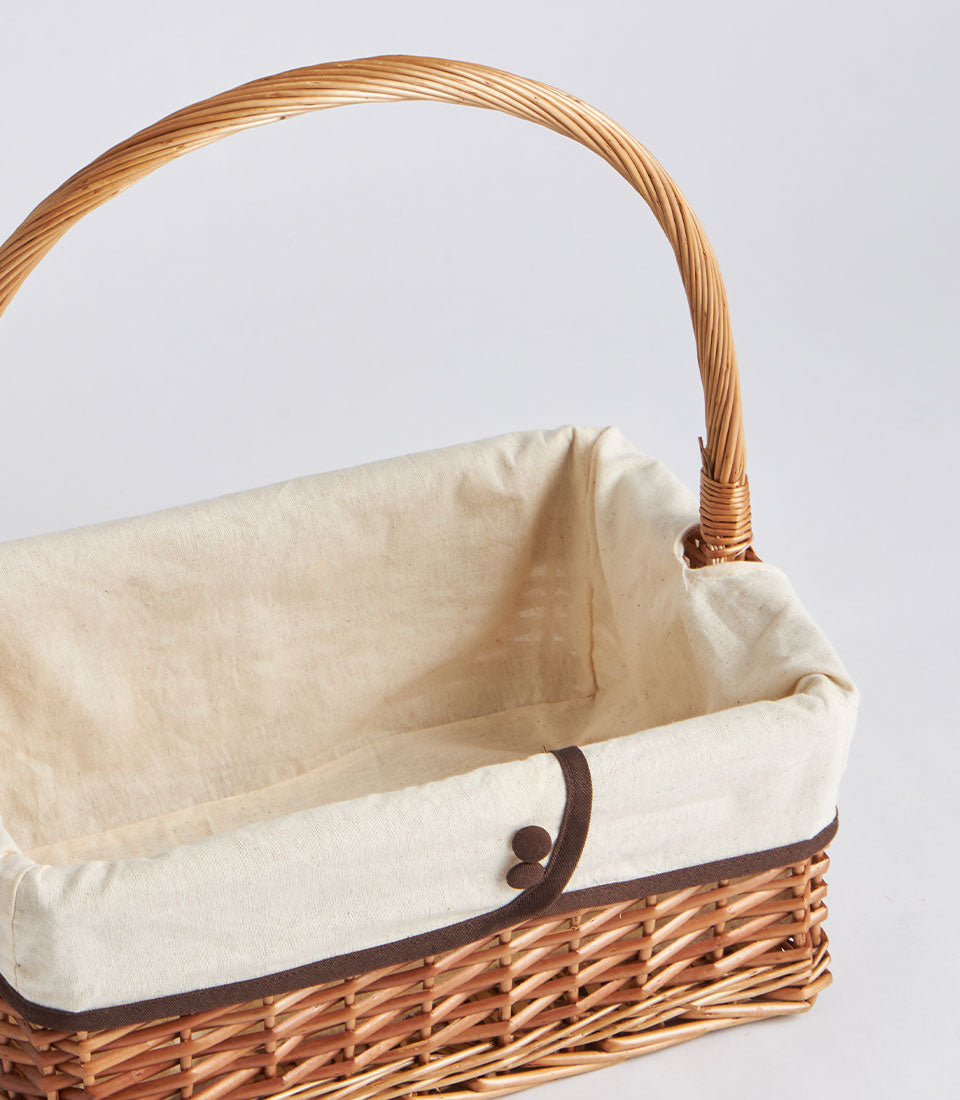 Handwoven rectangular wicker gift basket with cream fabric lining and twisted handle