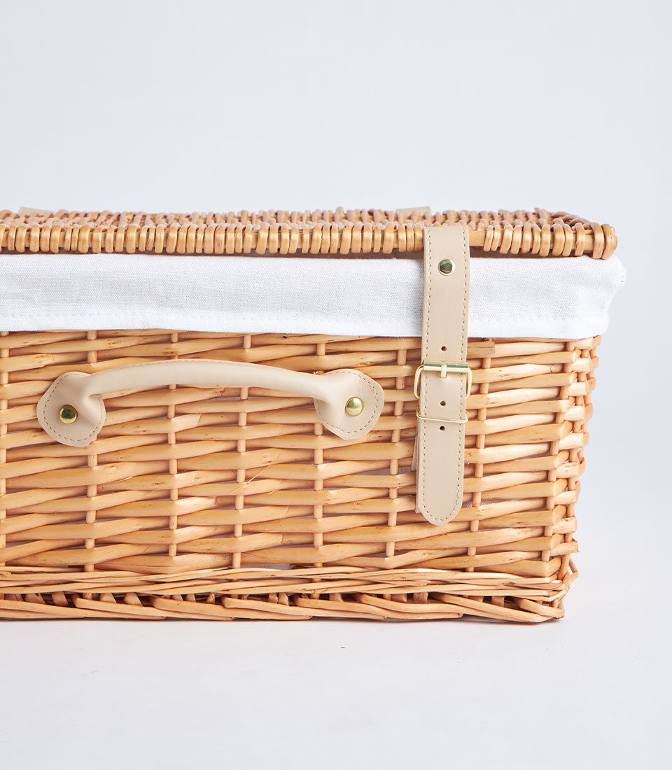 Handwoven rectangular rattan picnic basket with hinged lid, beige leather strap, and gold buckle