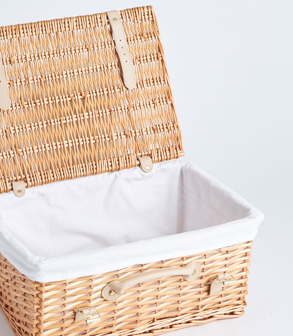 Light brown woven wicker picnic basket with cream linen lining, leather straps and gold hardware