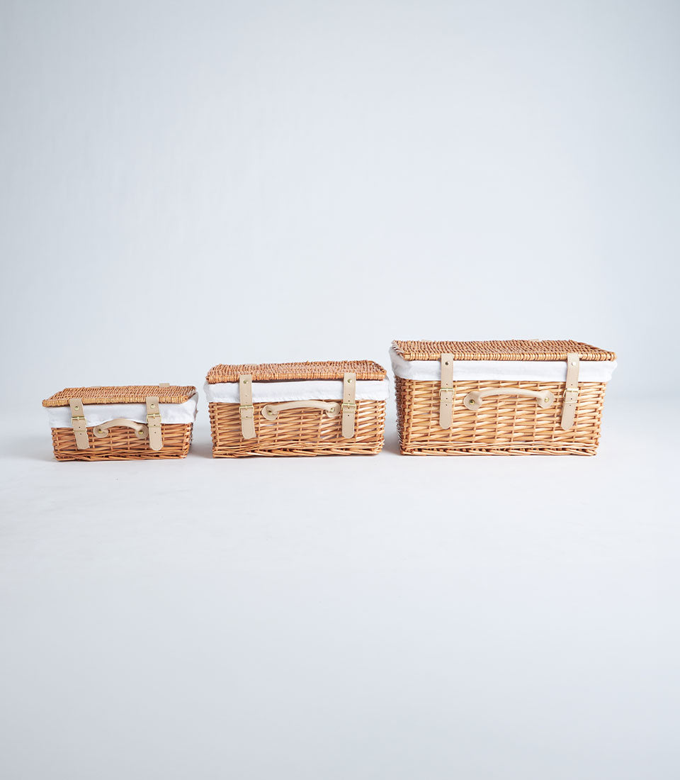 Handwoven wicker picnic baskets in natural tan with leather handles and brass buckle closures, three sizes