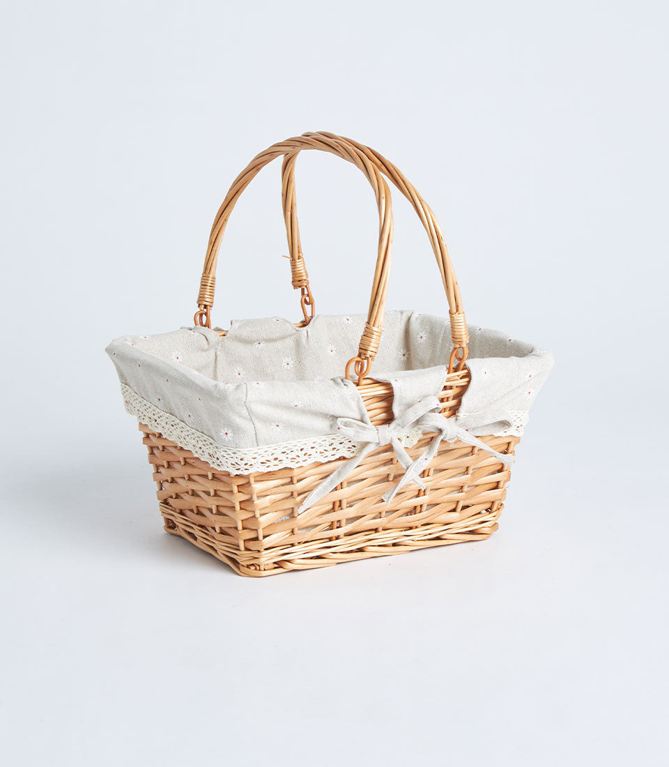 Handwoven rectangular wicker basket with dual handles, beige fabric lining, and delicate floral bow detail