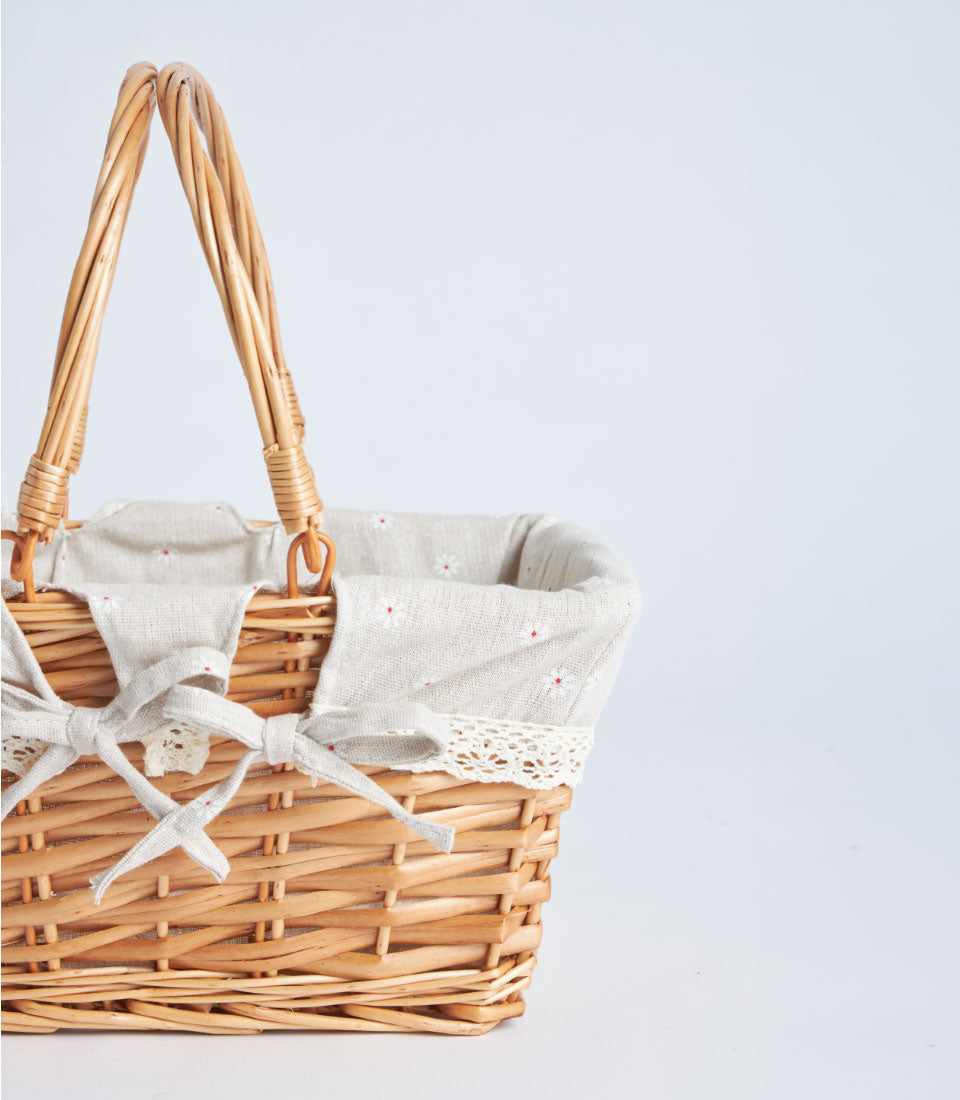 Light brown handwoven wicker basket with dual handles, beige floral fabric lining, and cream lace trim