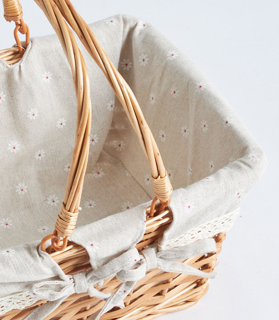 Light brown handwoven wicker basket with dual handles, beige floral fabric lining, and white lace trim