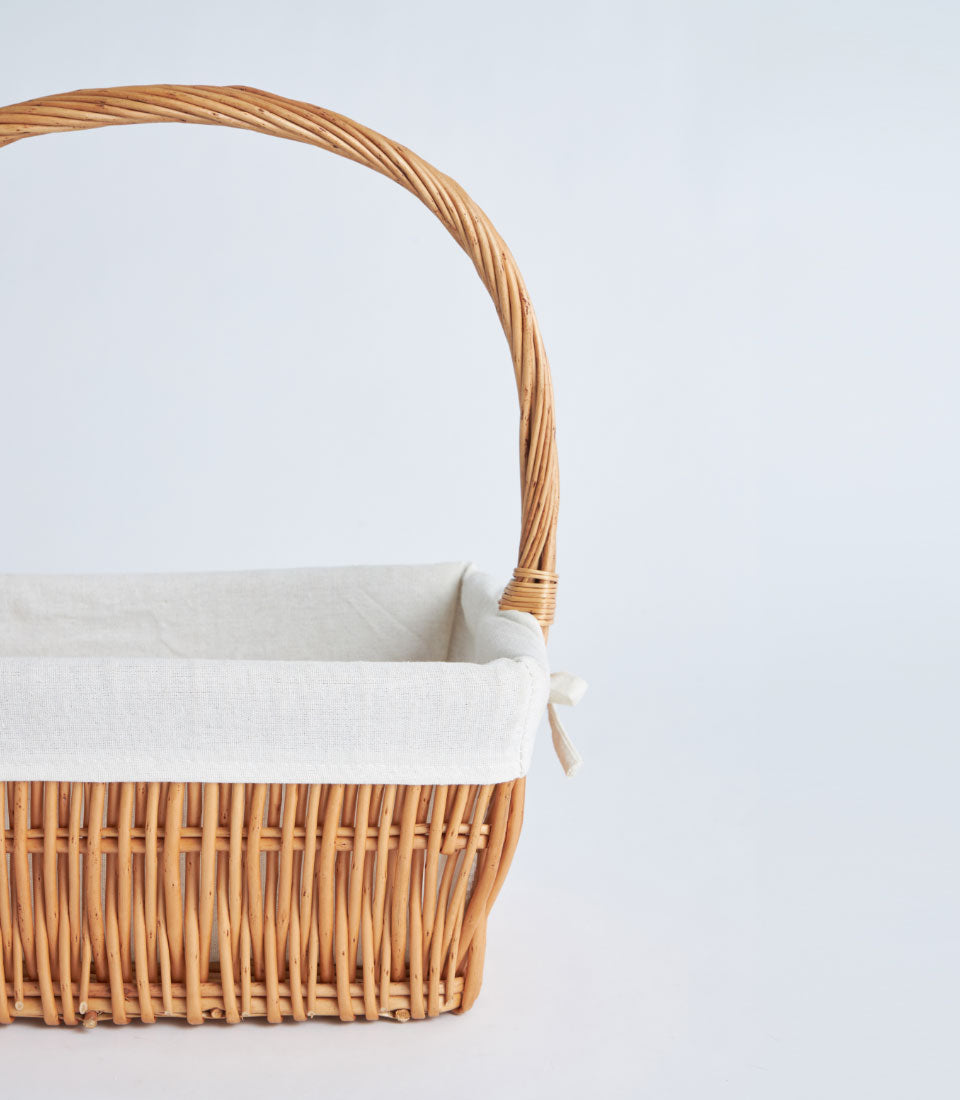 Light brown wicker rectangular basket with off-white fabric lining and arched handle