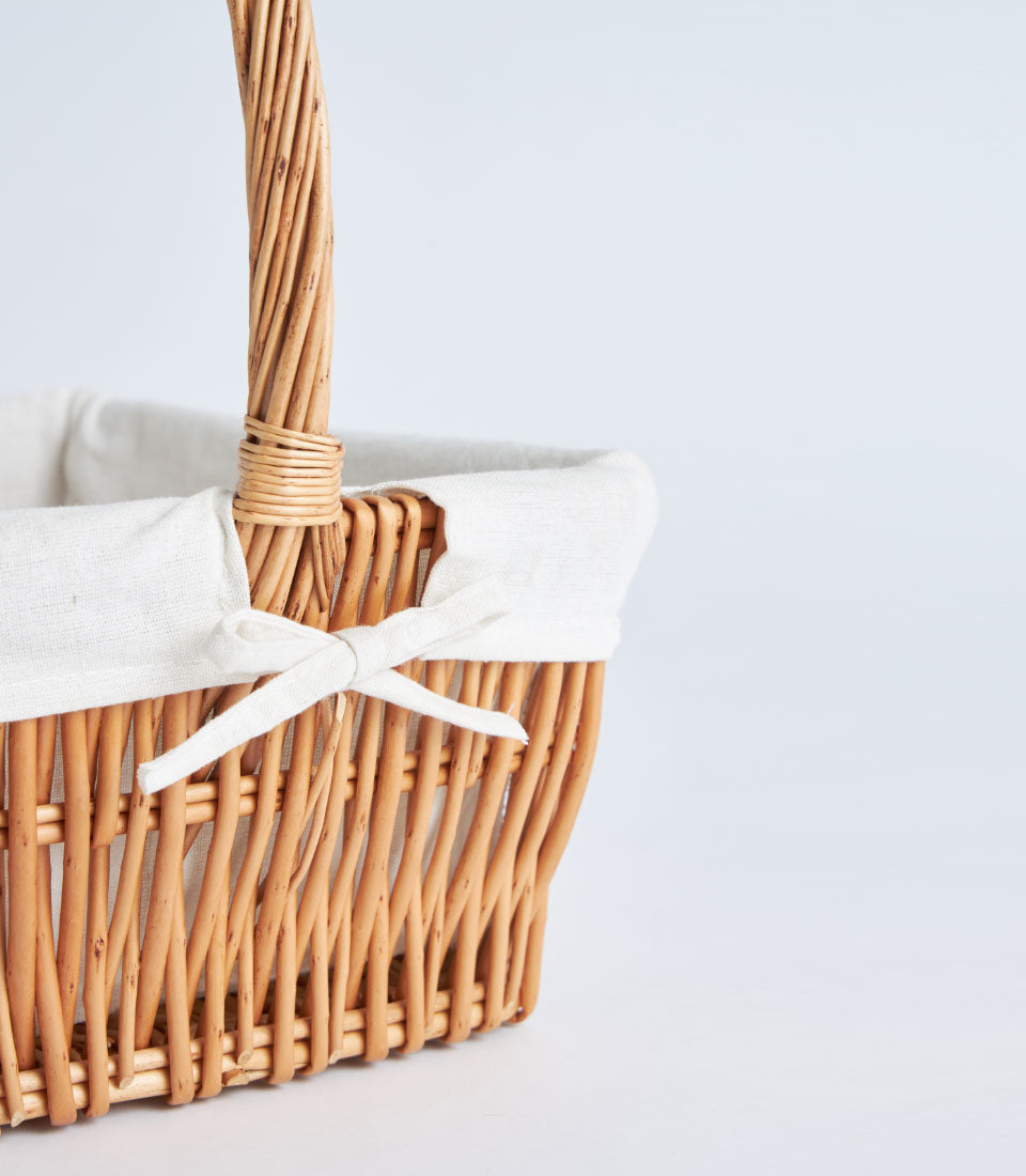 Light brown wicker rectangular gift basket with white fabric lining and natural woven handle