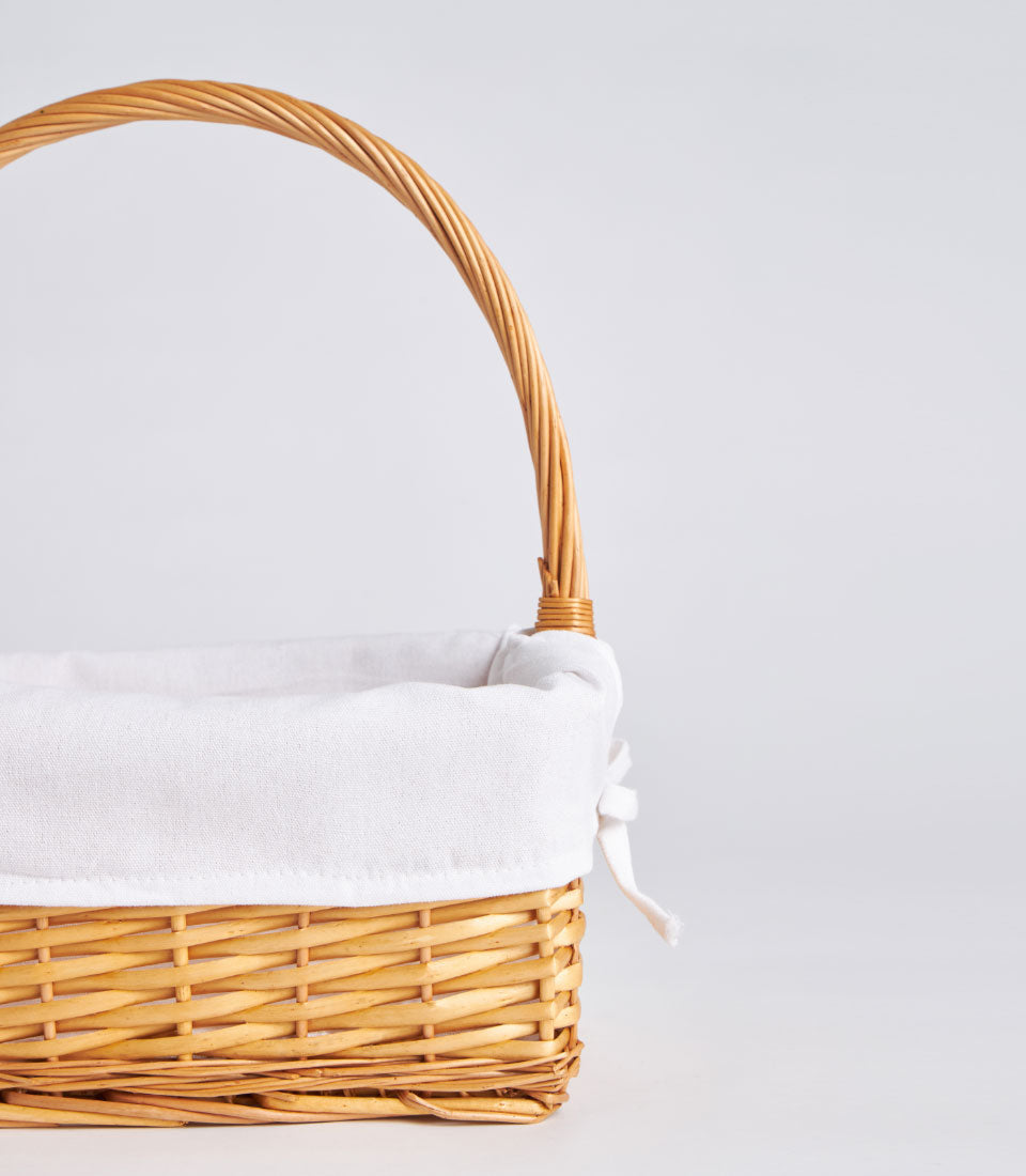 Light brown handwoven wicker basket with tall curved handle and white fabric lining