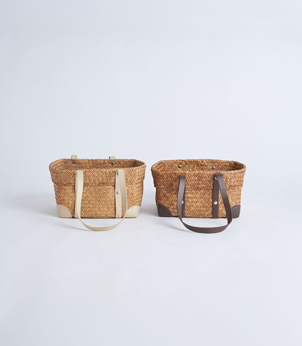 Natural woven oval baskets with leather strap handles in light beige and dark brown
