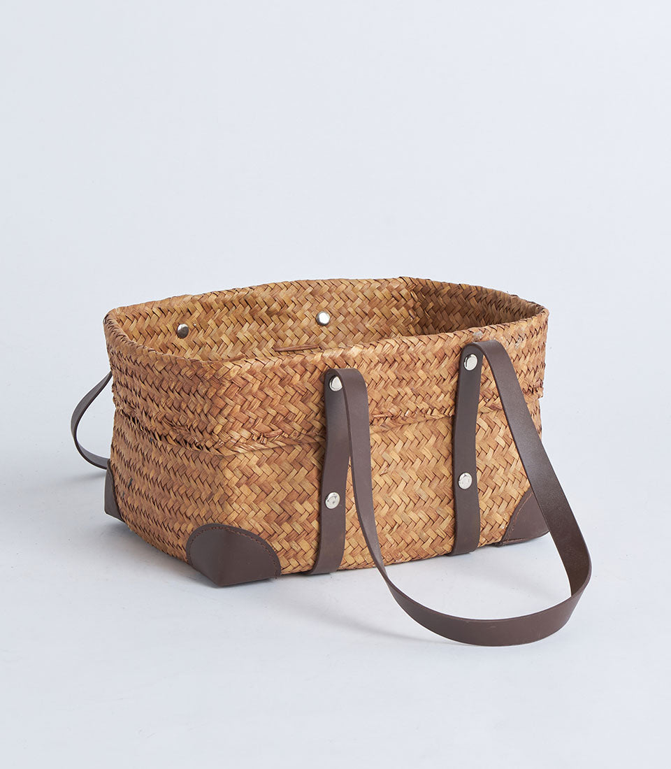 Natural woven straw basket with black faux leather handles and riveted accents