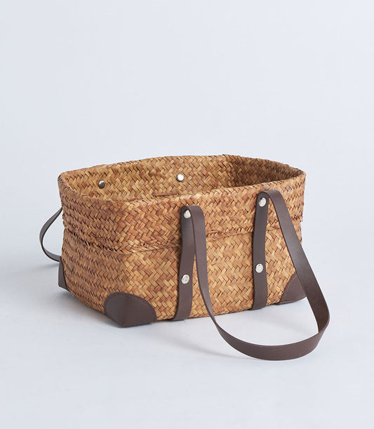 Natural woven straw basket with black faux leather handles and riveted accents