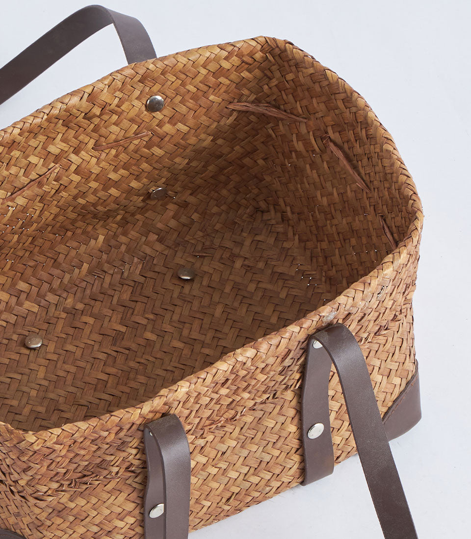 Natural woven straw basket with dark leather handles and metal rivets, perfect for premium gift presentation